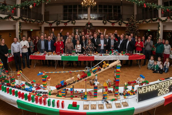 Freudige Gruppe bei einer Weihnachtsfeier im Hintergrund und fertige X-Mas Dominoeffekt Kettenreaktion von bo events im Vordergrund.