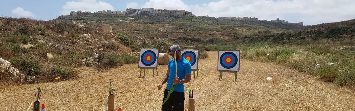 Ein Teamtrainer steht mit Recurvebogen in der Hand vor Zielscheiben. Bereit für Bogenschießen als Teamevent/Teambuilding/Betriebsausflug von bo events.