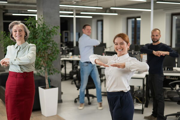 Vier Personen bei der Ausführung von Bewegungsübungen in einem Büro.