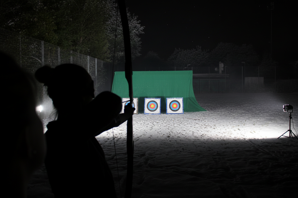 Person beim Zielen bei einem Nachtbogenschießen als Winter-Teamevent.