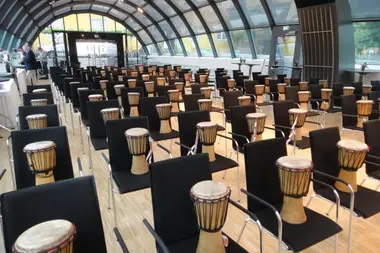 Viele Djembés auf Stühlen verteilt. Bereit für ein Team-Drumming-Event mit bo events.